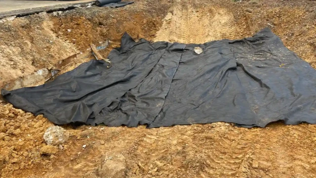 We are now preparing the first layer of soil to fill inside the area. The pool pit is now lined with a black geotextile fabric, likely for soil stabilization or drainage. The surrounding dirt walls still show signs of recent excavation.
